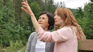 一位<strong>年迈</strong>的退休<strong>母亲</strong>和成年女儿正在树林茂密的山脉背景下交谈。 假期